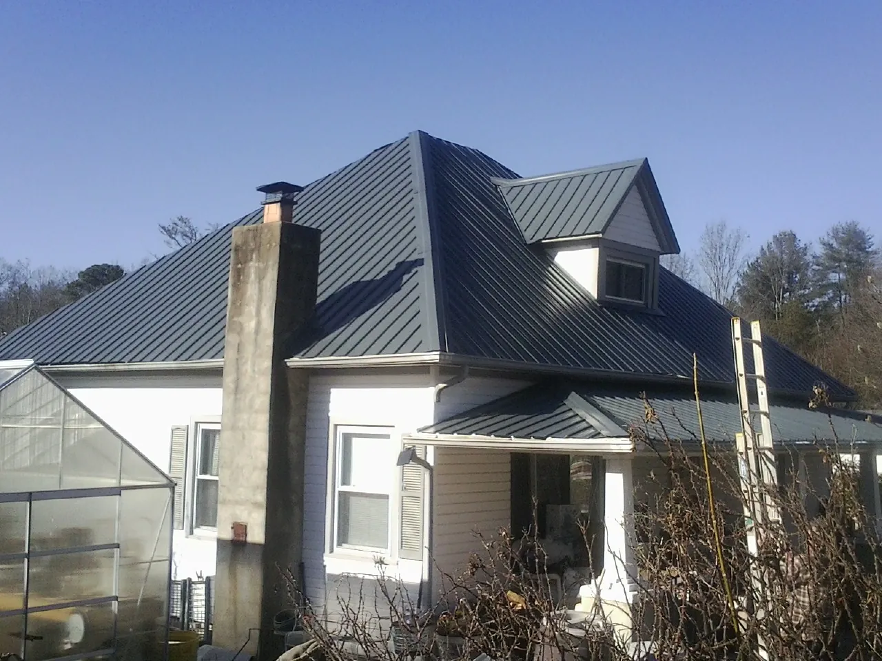 Dark blue standing seam metal roof on a white farmhouse with dormer — Slate & Tile Roof Repair by Roofing Brothers in Wixom