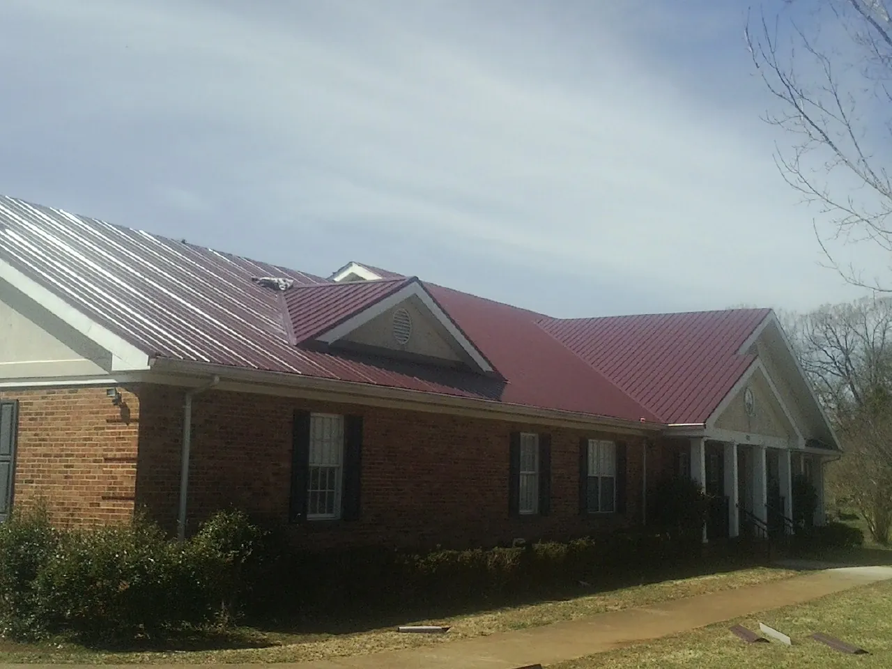 Red metal roof with gabled entries on a long brick building, from a Hail Damage Roof Repair job in Wixom