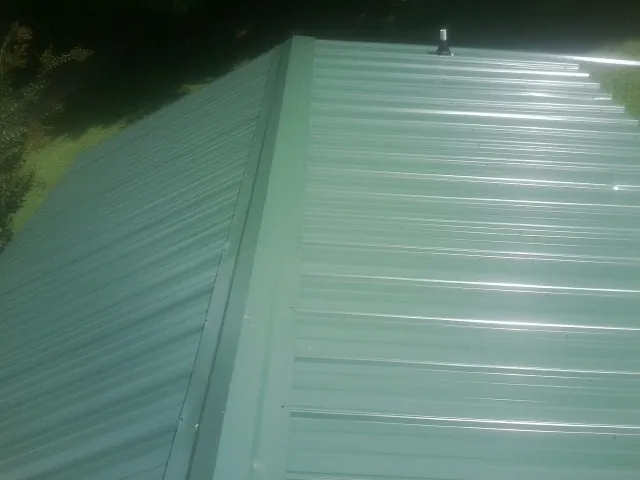 New green metal panels meeting at the ridge of a roof — Flat Roof Repair work by our crew in Wixom