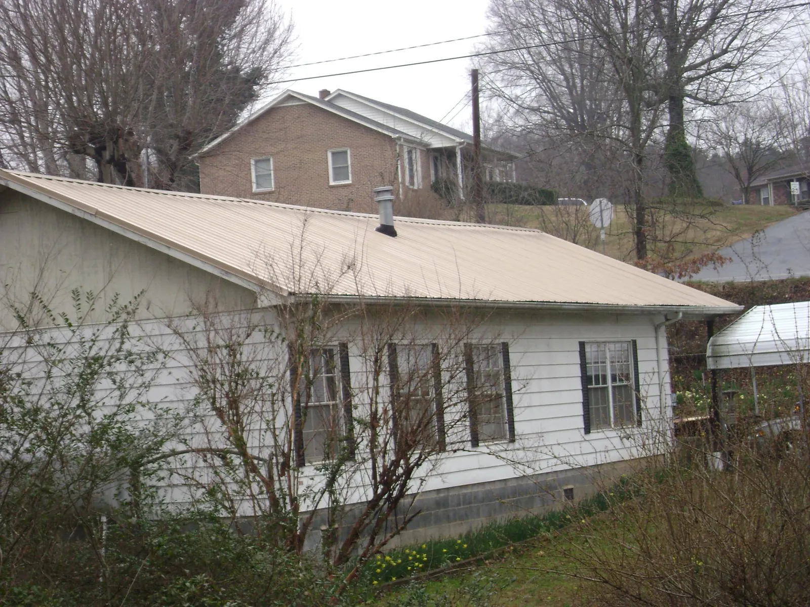 Tan metal roof on a white sided house set into a hillside — Commercial Roofing by Roofing Brothers in Wixom