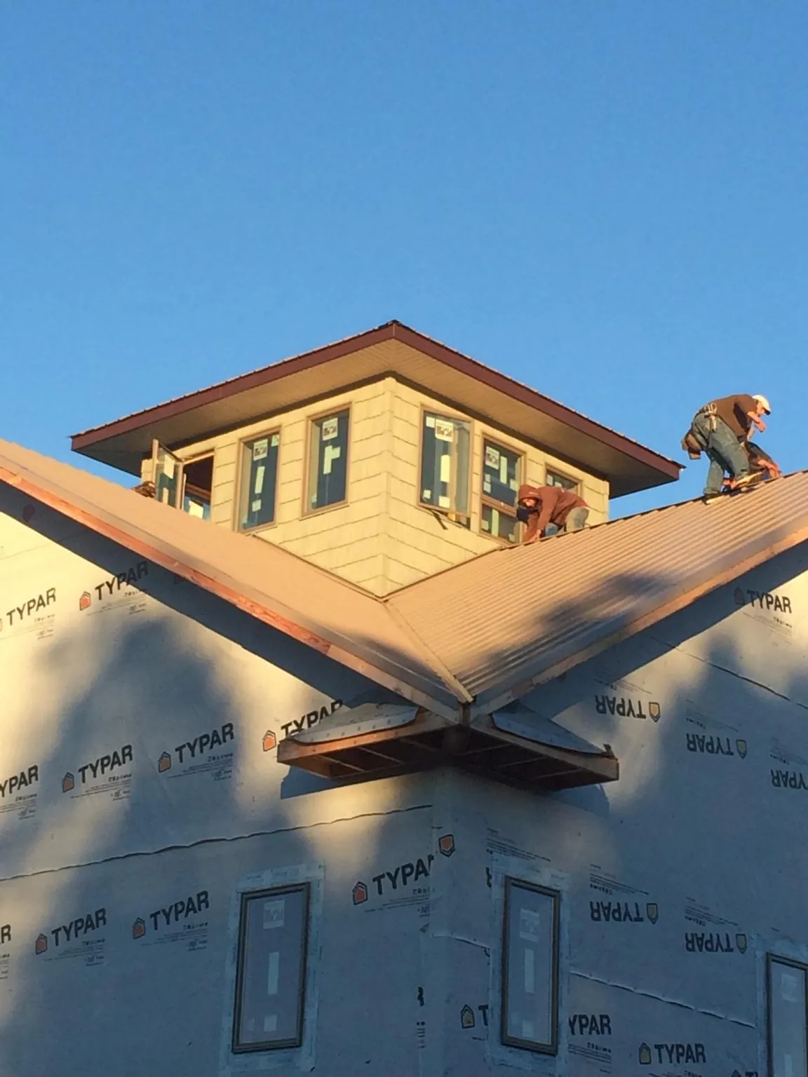 Roofers working around a rooftop cupola on a new metal roof at sunset — Roof Waterproofing in Wixom by Roofing Brothers